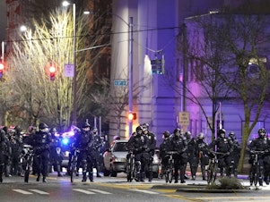 caption: Police and other law enforcement officials stand in a line as protesters approach in the street in front of the City-County Building on Sunday in Tacoma, Wash.