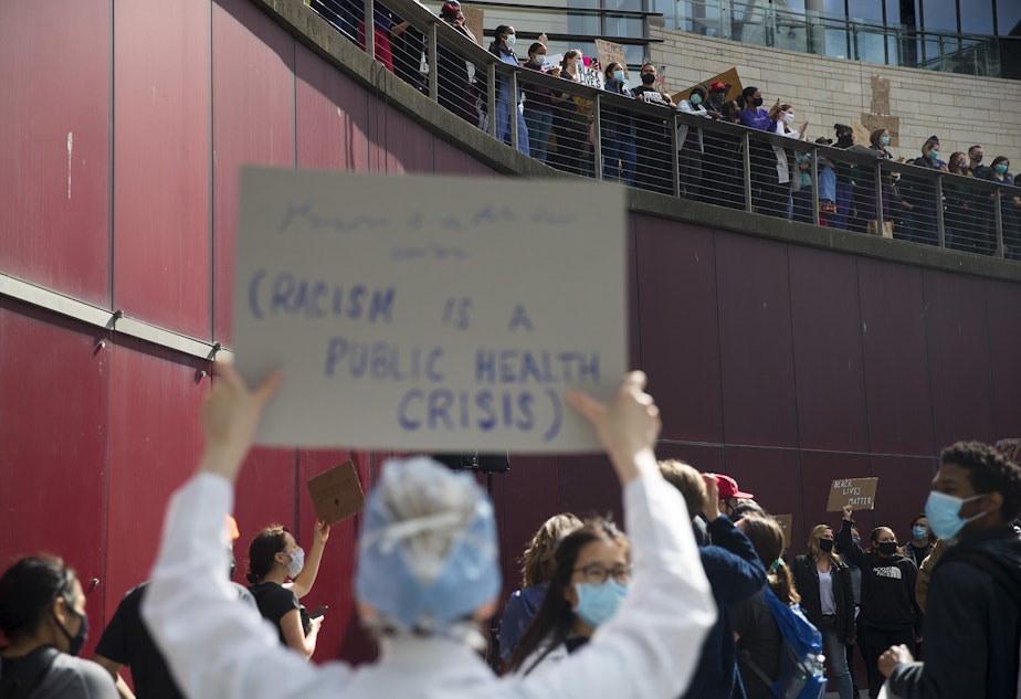 caption: A healthcare worker holds a sign that reads, 'Racism is a Public Health Crisis,' after thousands marched in protest of police violence and to demand justice for Black Americans unjustly killed at the hands of law enforcement, from Harborview Medical Center to Seattle City Hall on Saturday, June 6, 2020, in Seattle. 