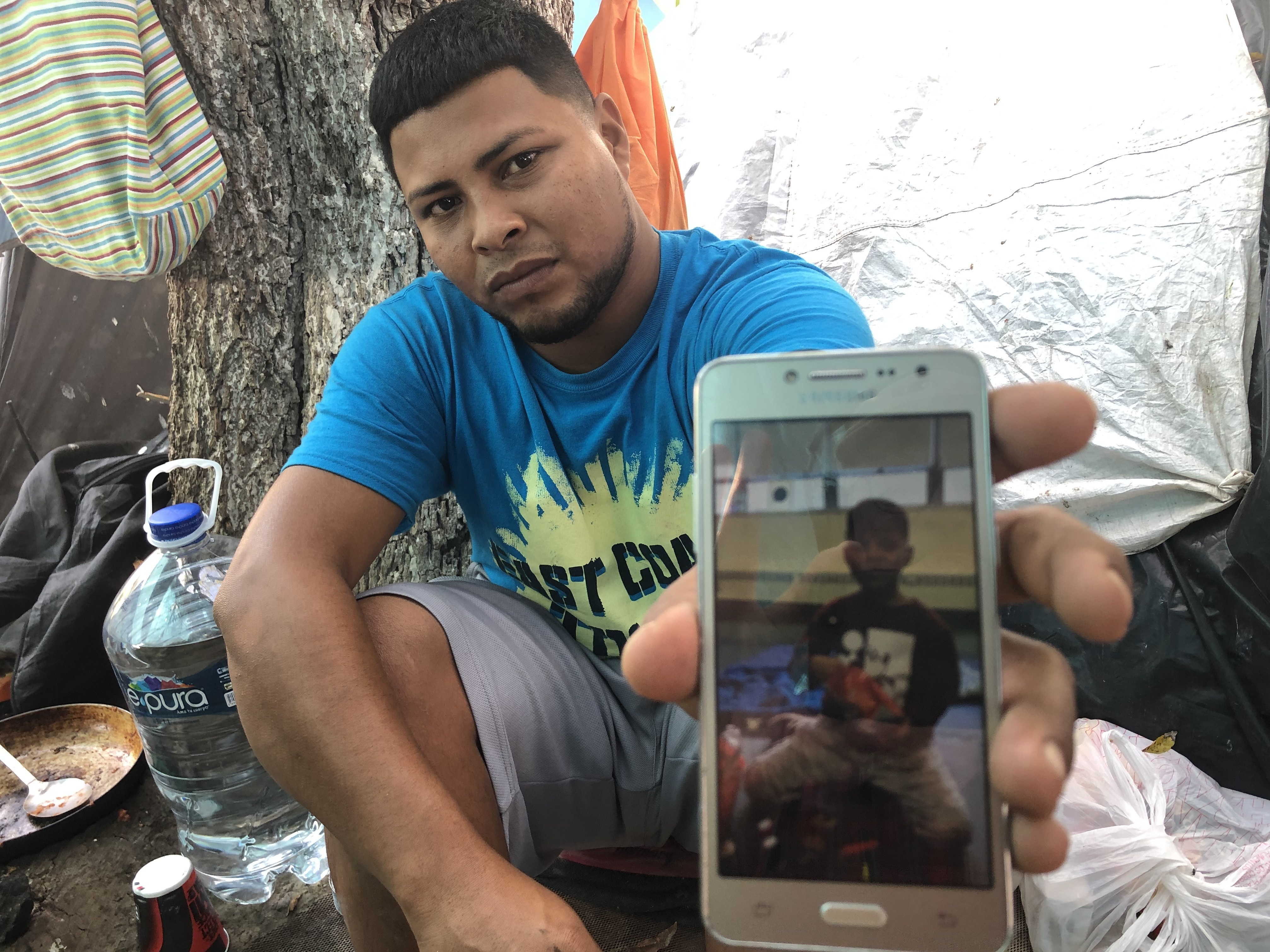 caption: Migrant parents in the tent camps in Matamoros, Mexico, are sending their kids across the border and taking advantage of the rule that unaccompanied children can't be returned to Mexico. Here,  Alexis Martinez holds a cellphone photo of his 7-year-old son Osiel.