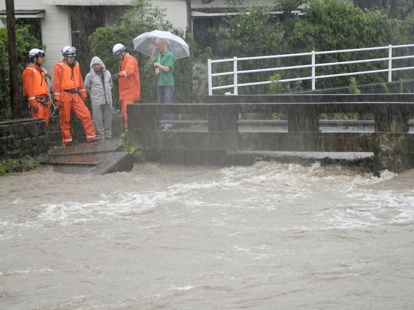 caption: Rescue workers and local residents watch the Wada River, which has been swollen due to heavy rain in Kagoshima, Japan. More than a million people in southwestern Japan are under evacuation orders due to torrential rains.
