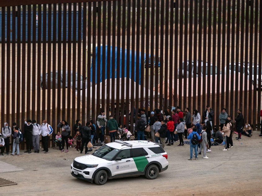 caption: Migrants and asylum seekers wait to be processed by the Border Patrol between fences at the US-Mexico border seen from Tijuana, Baja California state, Mexico, on June 5, 2024.