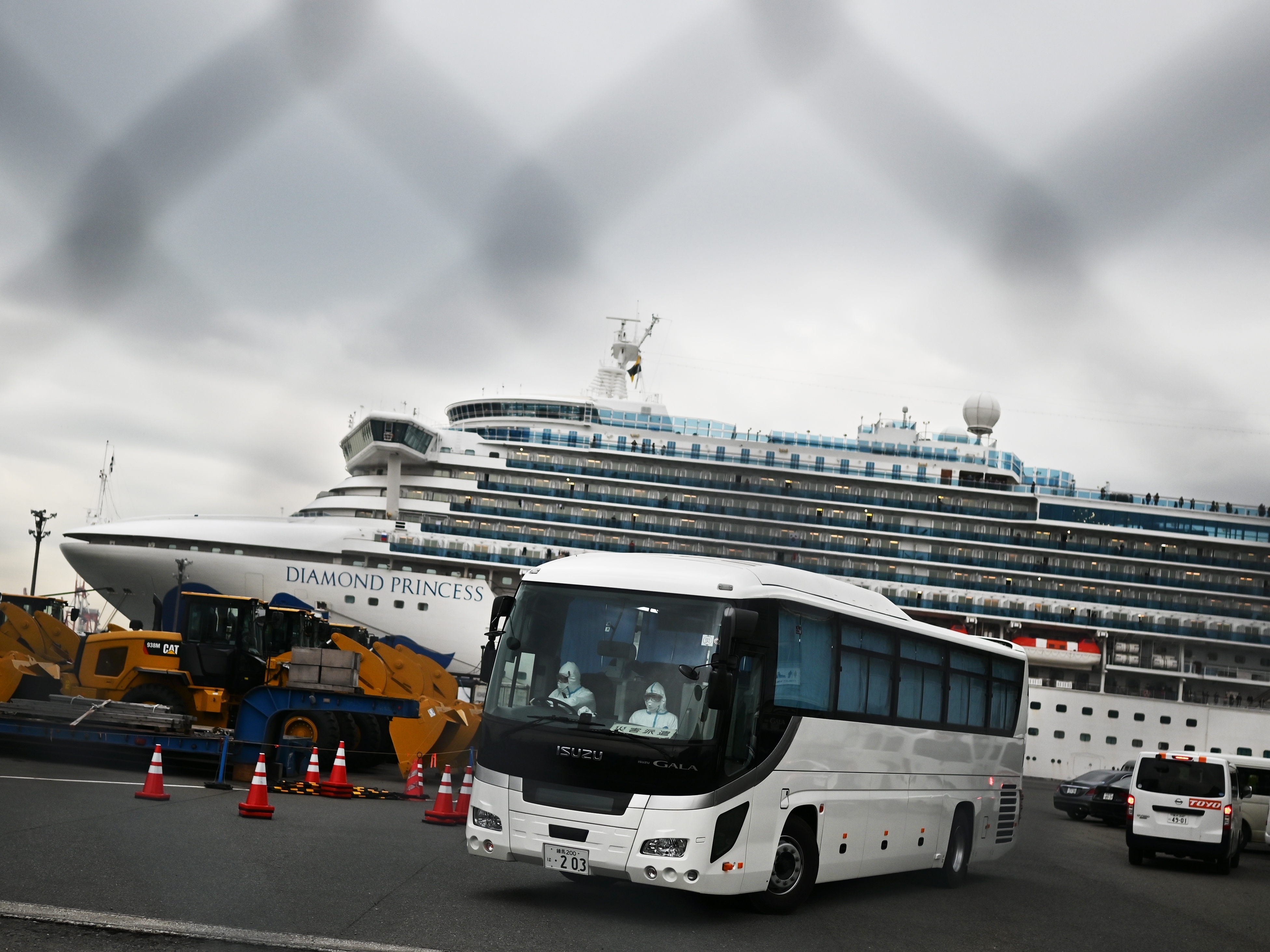 caption: A bus departs from the dock where the Diamond Princess cruise ship sits under quarantine with its thousands of passengers and crew. Japanese authorities said Friday that some older passengers who tested negative for the coronavirus were allowed to disembark.