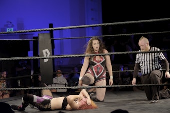 caption: Nicole Matthews kneels next to a fallen Masha Slamovich during DEFY Wrestling's "Violent Minds"