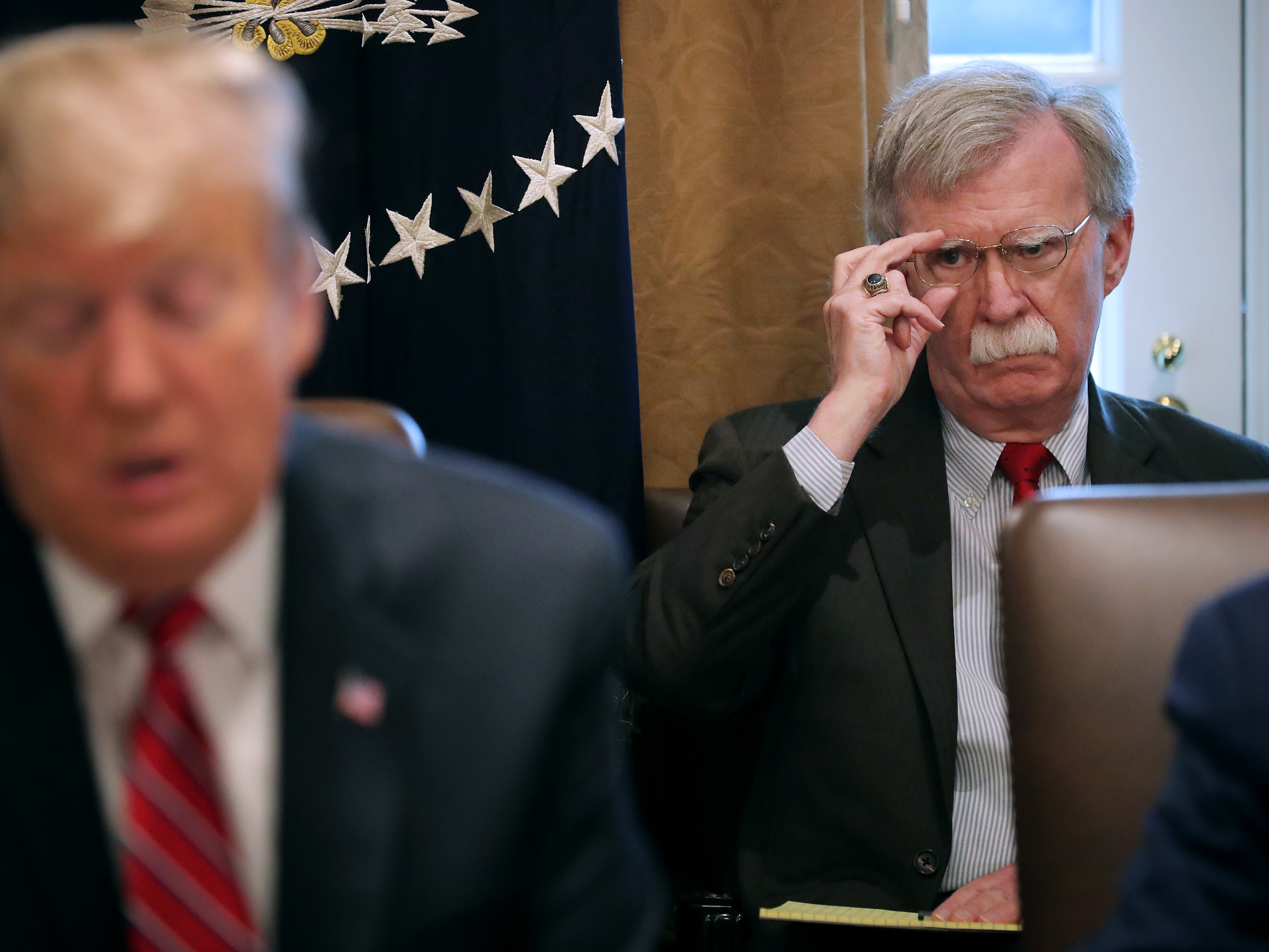 caption: Then-National Security Advisor John Bolton (R) listens to President Trump talk to reporters at the White House in February 2019 in Washington, DC.