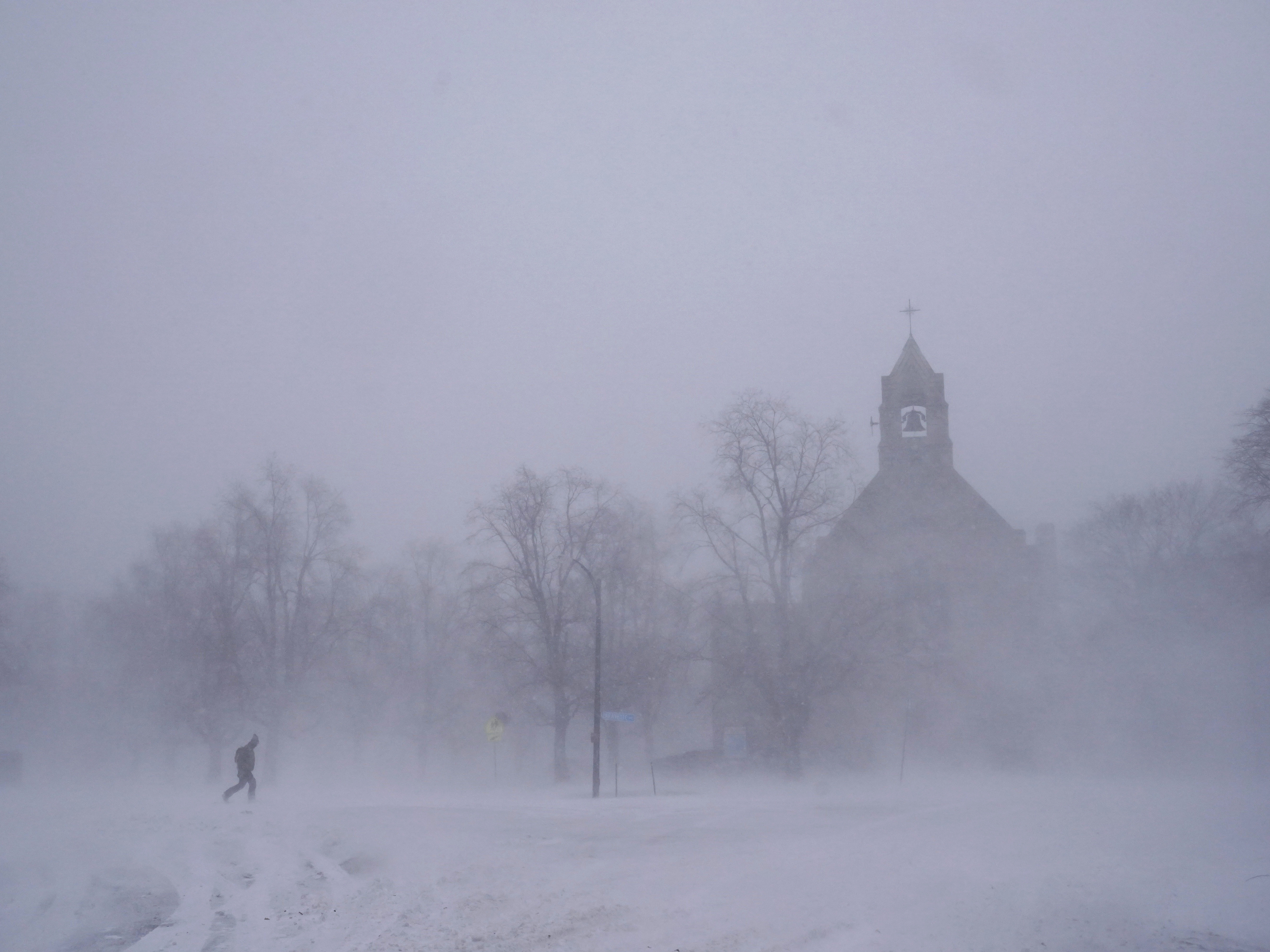 caption: A lone pedestrian in snow shoes makes his way across Colonial Circle as St. John's Grace Episcopal Church rises above the blowing snow amid blizzard conditions in Buffalo, N.Y. on Saturday.