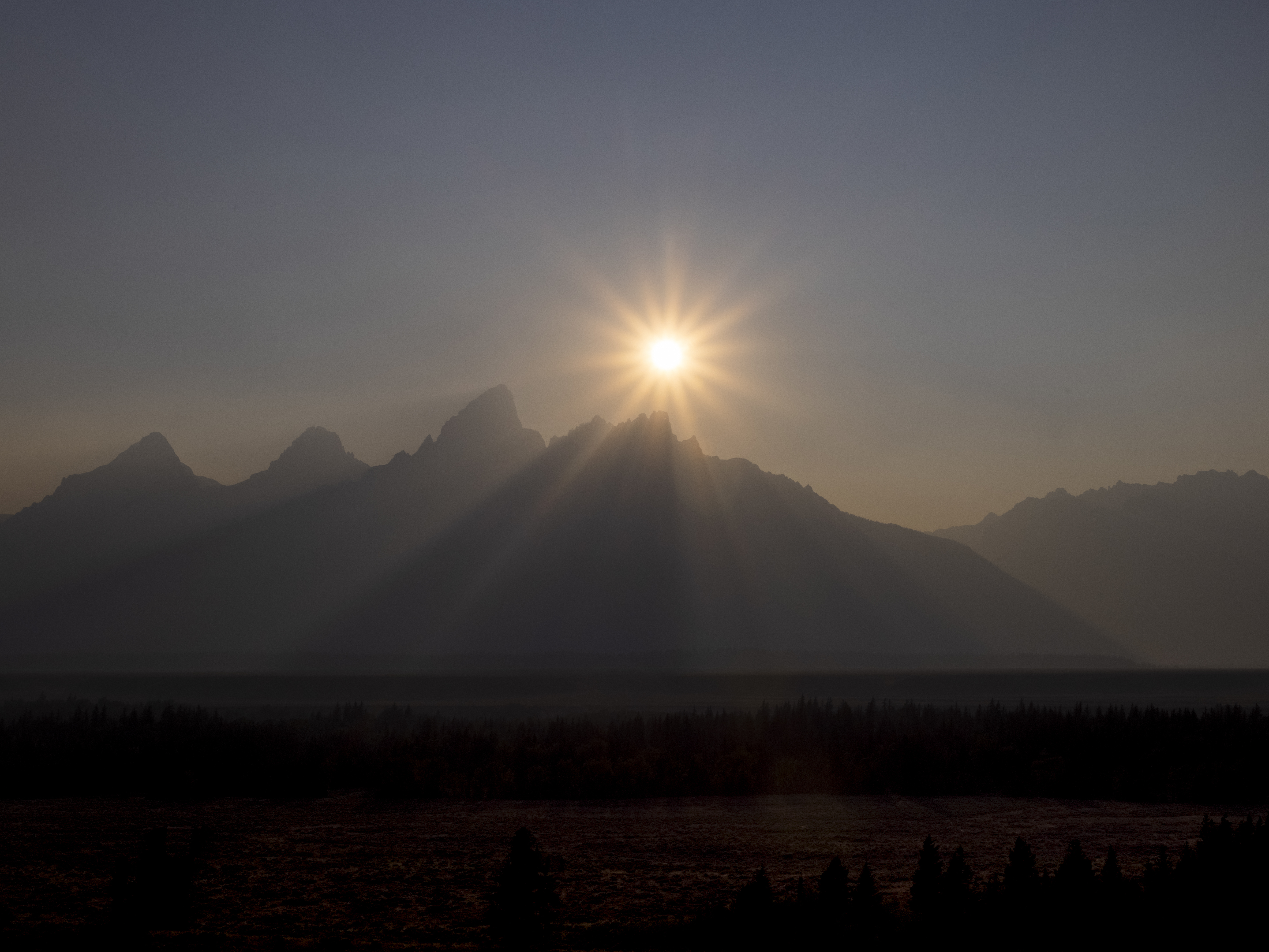 caption: A peak is shrouded in smoke from regional wildfires on July 14, at Grand Teton National Park, south of Yellowstone.