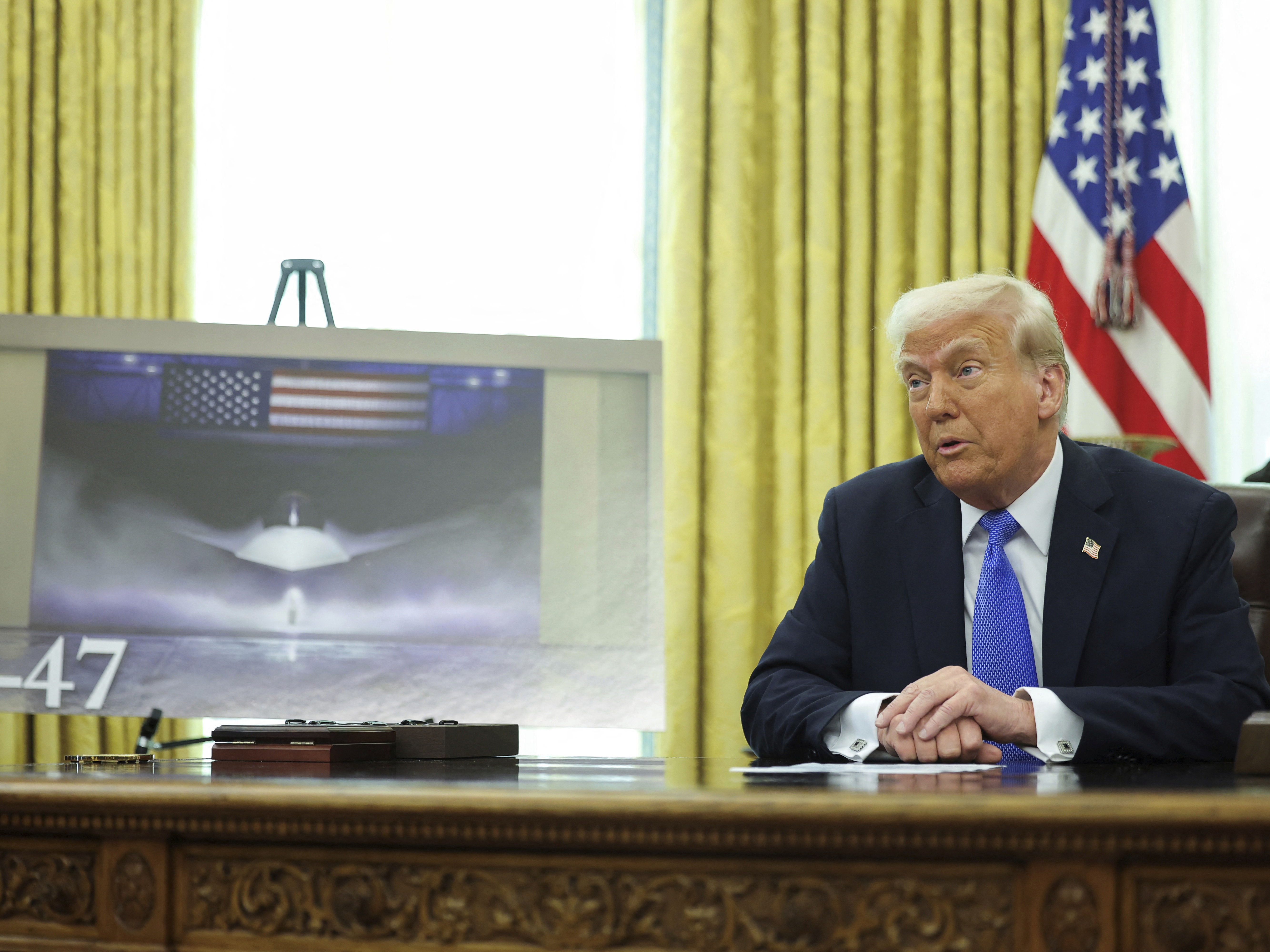 caption: President Trump speaks as an image of an F-47 fighter jet is displayed in the Oval Office in Washington on Friday.