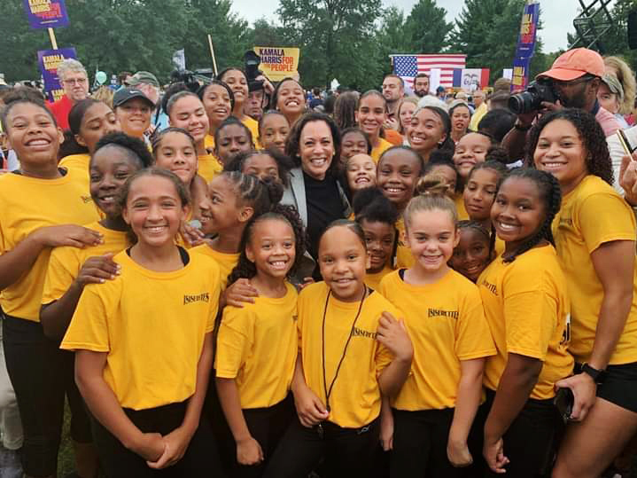 caption: Kamala Harris poses with the Isiserettes, a legendary drill-and-drum team, at the Polk County Steak Fry in Iowa in 2019.