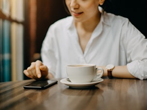 A young woman sits in cafe while text messaging on smartphone.