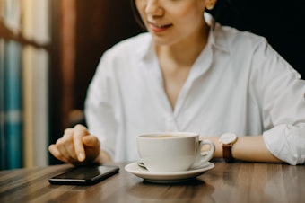 A young woman sits in cafe while text messaging on smartphone.