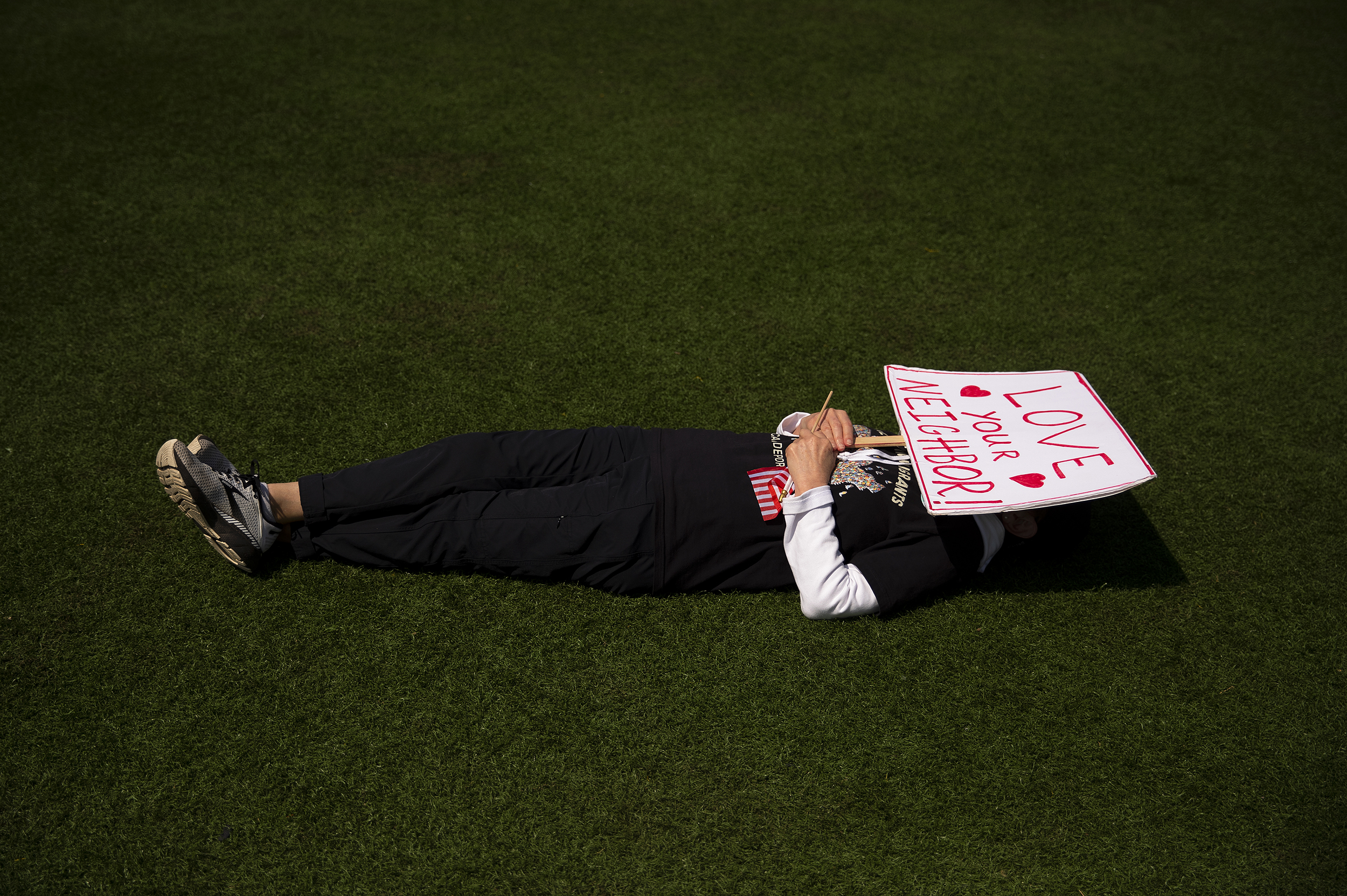 caption: A handmade sign reading ‘Love Your Neighbor’ shields a demonstrator from the sun during the annual May Day rally on Friday, May 1, 2026, at Cal Anderson Park in Seattle. 