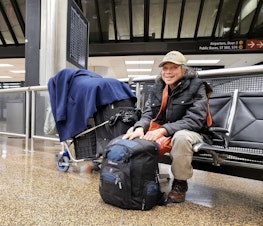 caption: De Chung sits with his bags and belongings near a luggage carousel at SeaTac Airport on Tuesday, Jan. 3, 2023.