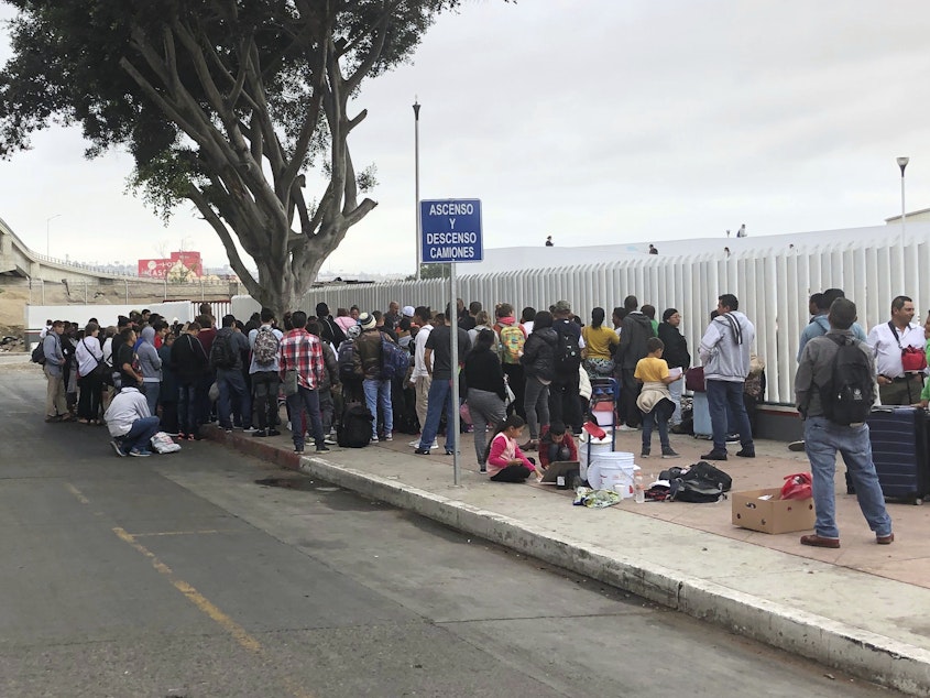 caption: Asylum seekers in Tijuana, Mexico, listen to names being called from a waiting list to claim asylum at a border crossing in San Diego on Sept. 26.