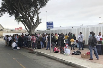 caption: Asylum seekers in Tijuana, Mexico, listen to names being called from a waiting list to claim asylum at a border crossing in San Diego on Sept. 26.