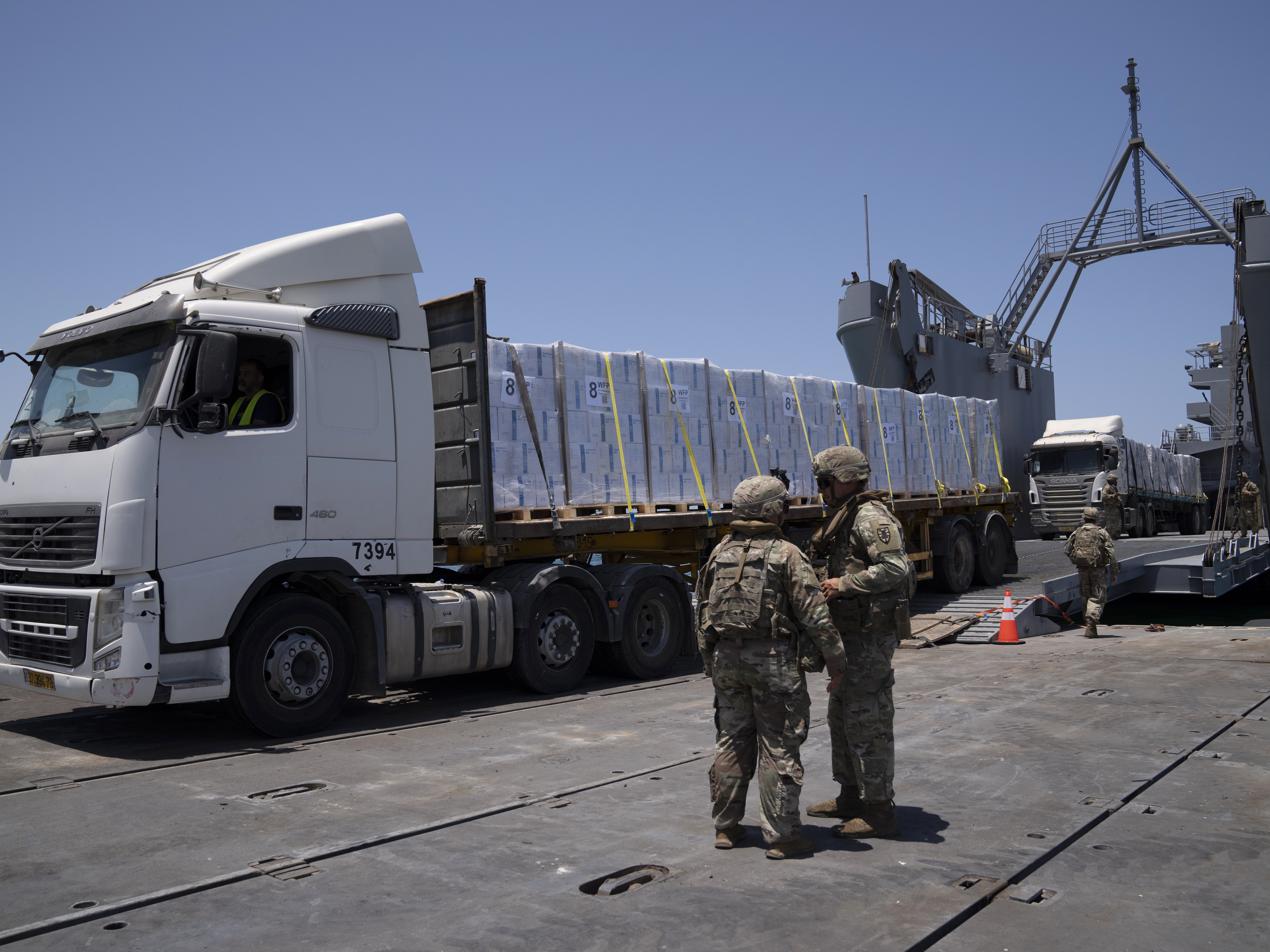 caption: U.S. Army soldiers stand next to trucks arriving loaded with humanitarian aid at the U.S.-built floating pier Trident before reaching the beach on the coast of the Gaza Strip, June 25, 2024.