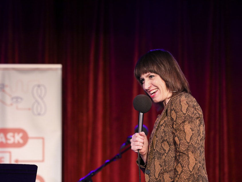 caption: Ophira Eisenberg performs on stage on <em>Ask Me Another</em> at the Bell House in Brooklyn, New York.