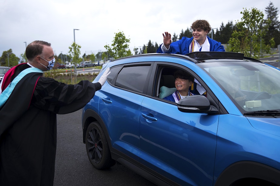 caption: Federal Way Principal Dr. Matt Oberst, left, waves goodbye to seniors Jinsu Ha, center, and Alex Bradshaw, upper right, after they participated in the filming of a graduation walk video to be used in an upcoming virtual graduation ceremony, on Wednesday, May 20, 2020, at Federal Way High School. “I don’t feel like my chapter in high school is fully ended," said Ha. "I wasn’t ready to finish it yet, but it’s somehow already over.”