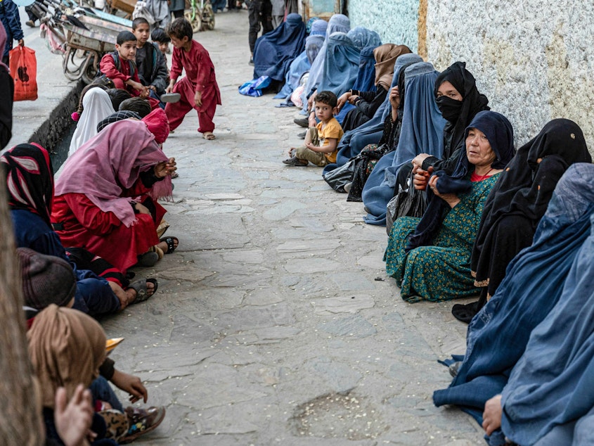 caption: Afghan women wait for a free bread. Charities allege that the Taliban interferes with their distribution of aid by pressuring them to funnel money to the Taliban and its supporters.