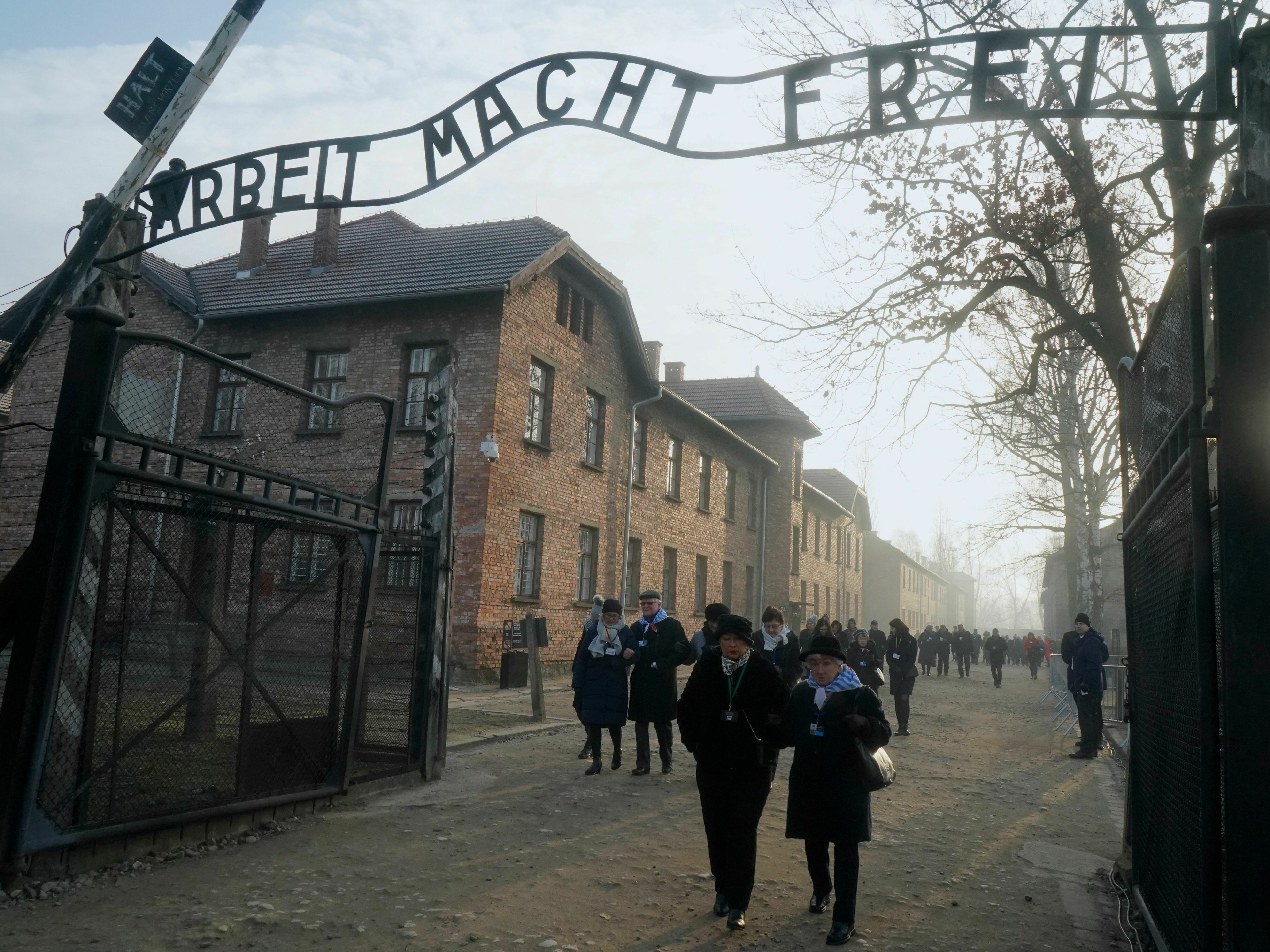 caption: In this 2020 photo, survivors walk below a gate with the inscription "Work sets you free" after a wreath-laying ceremony at the memorial site of the former German Nazi death camp Auschwitz during ceremonies marking the 75th anniversary of the camp's liberation in Oswiecim, Poland.