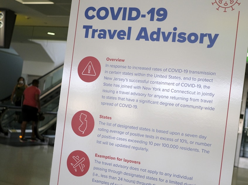 caption: A sign at Newark Liberty International Airport warns airline passengers about a travel advisory that applies to people arriving from certain states. Visitors from Alabama, Arkansas, Arizona, California, Florida, Georgia, Iowa, Idaho, Louisiana, Mississippi, Nevada, North Carolina, South Carolina, Tennessee, Texas and Utah should self-quarantine for two weeks.
