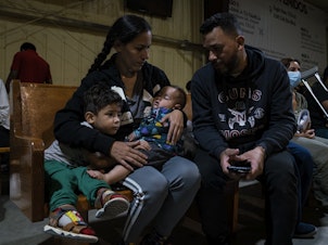 caption: Venezuelan migrants Kimberly González and Denny Velasco and their children wait for a bus at Mission: Border Hope in Eagle Pass, Texas.