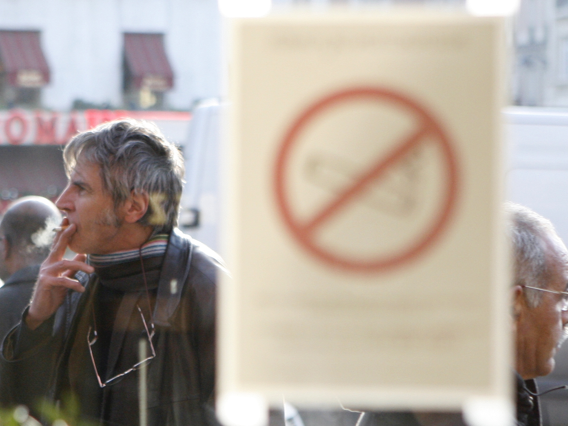 caption: A man smokes a cigarette outside a brasserie, in front of a sticker on a window reading: "Smoking is forbidden."