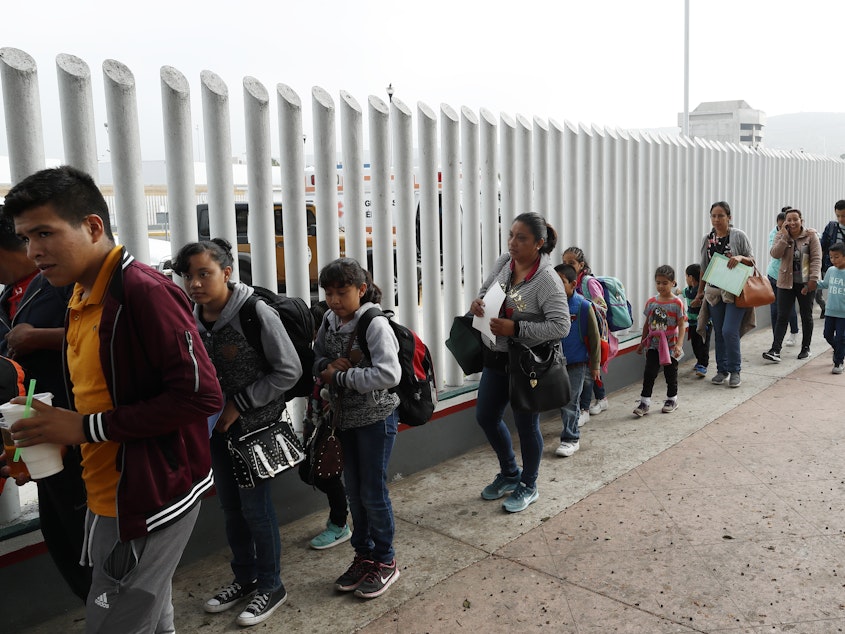 caption: People line up to cross into the United States to begin the process of applying for asylum near the San Ysidro Port of Entry in Tijuana, Mexico. President Trump has threatened to close the border to asylum-seekers.