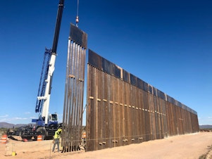 caption: A 30-foot border barrier — as tall as a two-story building — rises from the desert near Lukeville, Ariz.