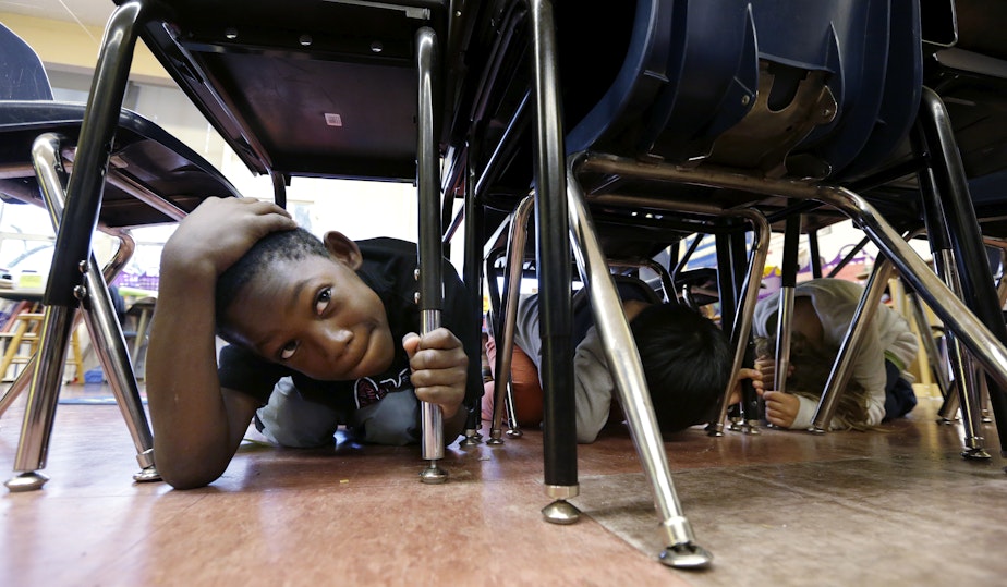 caption: A student covers his head and holds onto a table during a statewide earthquake drill, at Lowell Elementary School Thursday, Oct. 20, 2016, in Seattle. Schools, businesses, and community organizations conducted similar exercises across the state Thursday as part of the annual Great Washington ShakeOut earthquake and tsunami readiness program. 