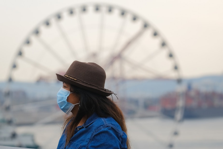 caption: A masked tourist walks through Pike Place Market, Tuesday, August 3, 2021.