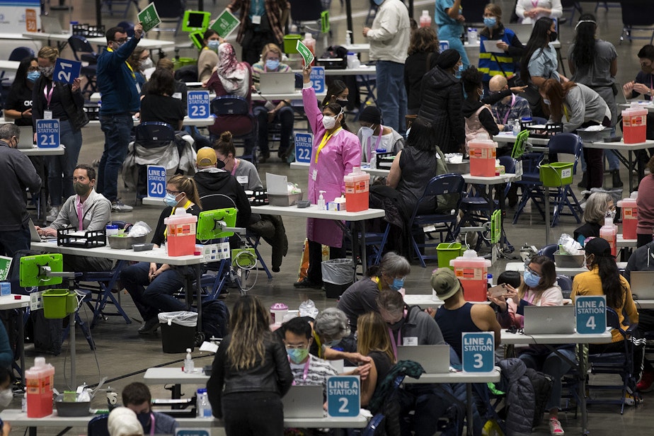 caption: Volunteer Dr. Aditi Agardwal, center in pink, raises a piece of paper indicting that she needs more vaccine on Saturday, March 13, 2021, at the new civilian-led mass Covid-19 vaccination site at Lumen Field Event Center in Seattle.