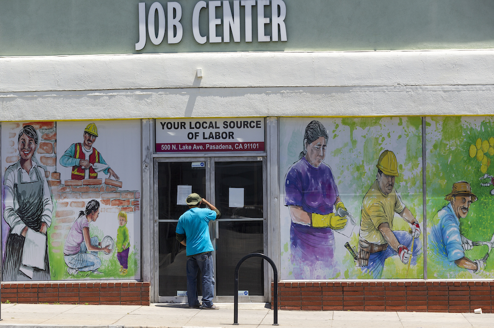 caption: A worker looks inside the closed doors of the Pasadena Community Job Center in Pasadena, Calif.,  Thursday, May 7, 2020, during the coronavirus outbreak. (Damian Dovarganes/AP Photo)