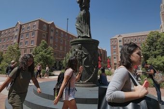 caption: Students walk by the statue of Hecuba, the legendary Queen of Troy, with a quote by William Shakespeare — spelled "Shakespear" — on the campus of the University of Southern California in Los Angeles in 2017.