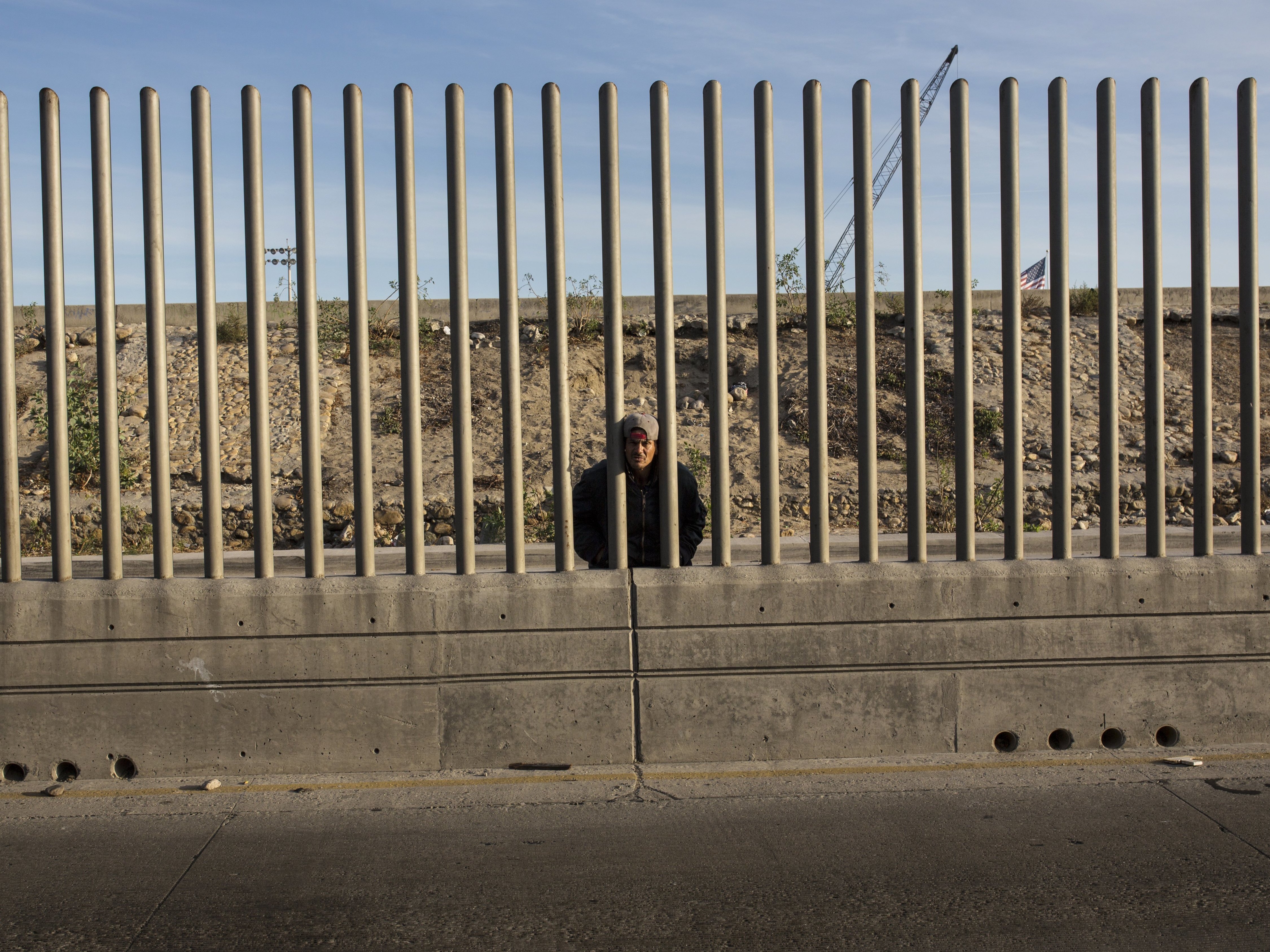 caption: Issac Rodriguez, from Sinaloa, Mexico, peering through the fence that divides Mexico and the U.S. in Tijuana, Mexico.