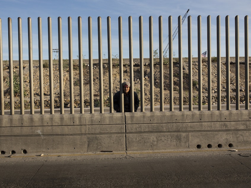 caption: Issac Rodriguez, from Sinaloa, Mexico, peering through the fence that divides Mexico and the U.S. in Tijuana, Mexico.
