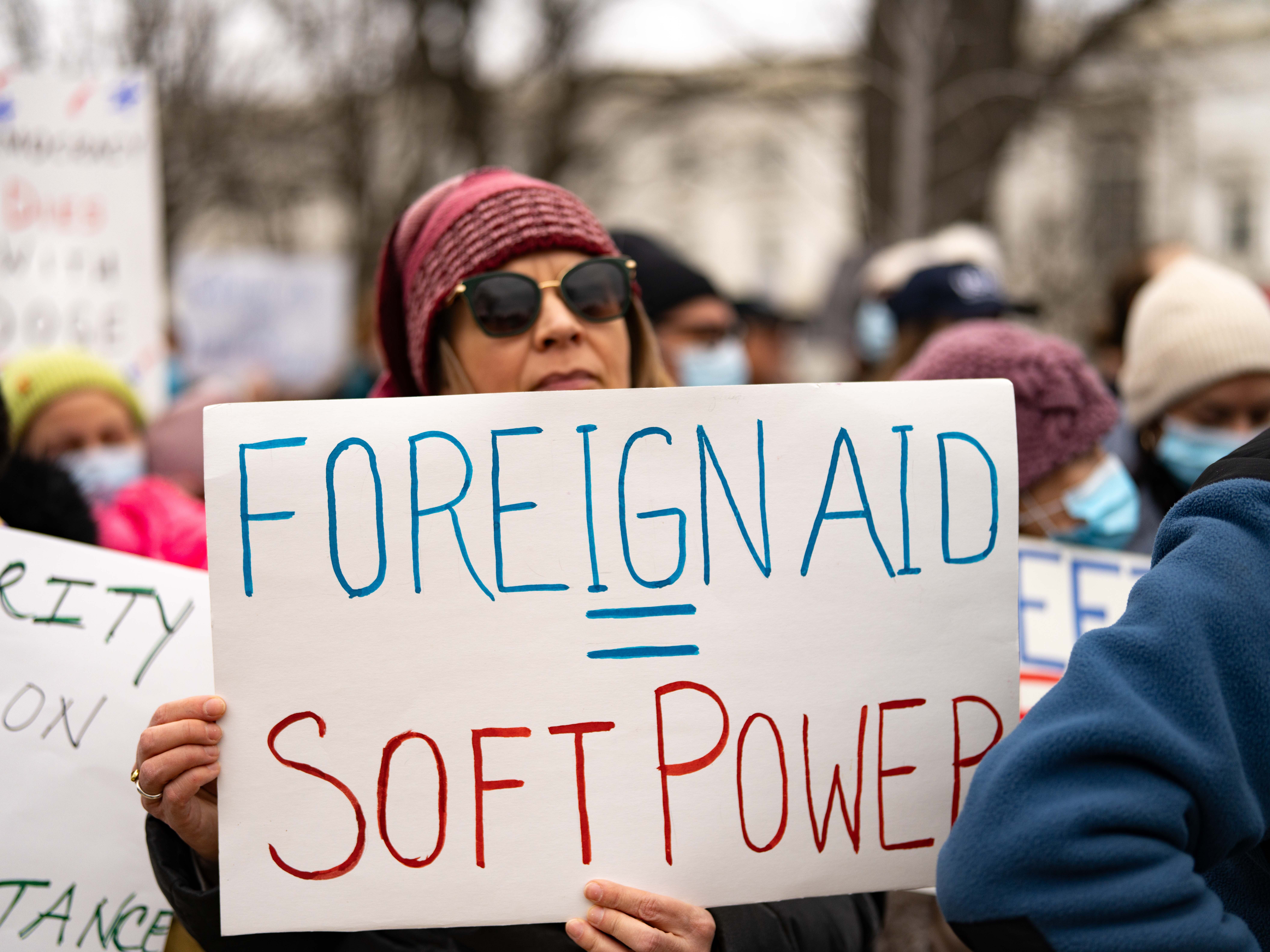caption: A protester carries a sign that equates foreign aid with soft power during a rally near the U.S. Capitol to protest the dismantling of USAID, the international agency charged with dispensing humanitarian aid around the world on behalf of the United States.