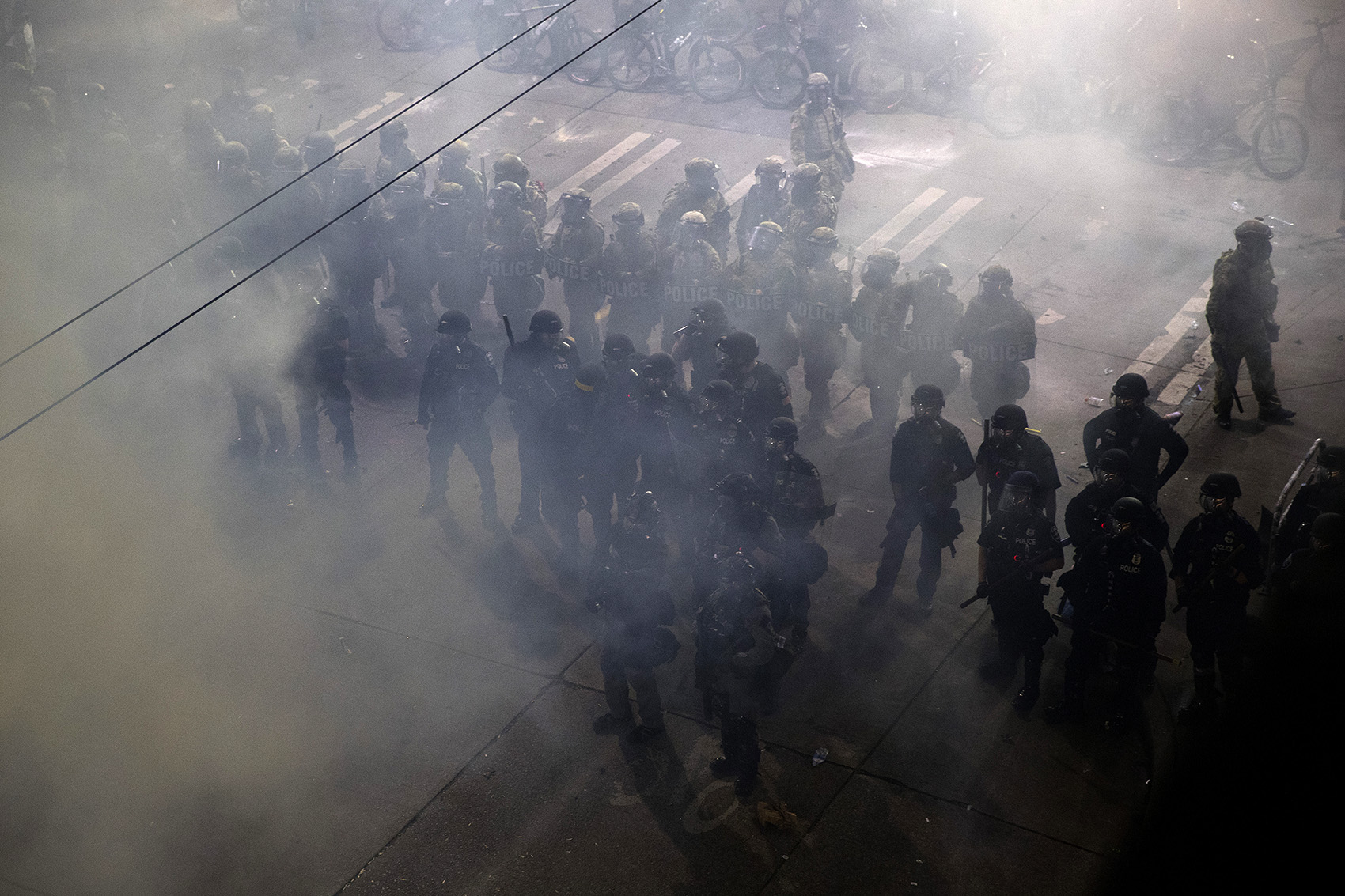 caption: Seattle police officers stand at the intersection of East Pine Street and 11th Avenue after deploying chemical agents, pepper spray and flash-bang grenades on demonstrators on the 10th day of protests following the police killing of George Floyd shortly after midnight on Monday June 8, 2020, in Seattle. 