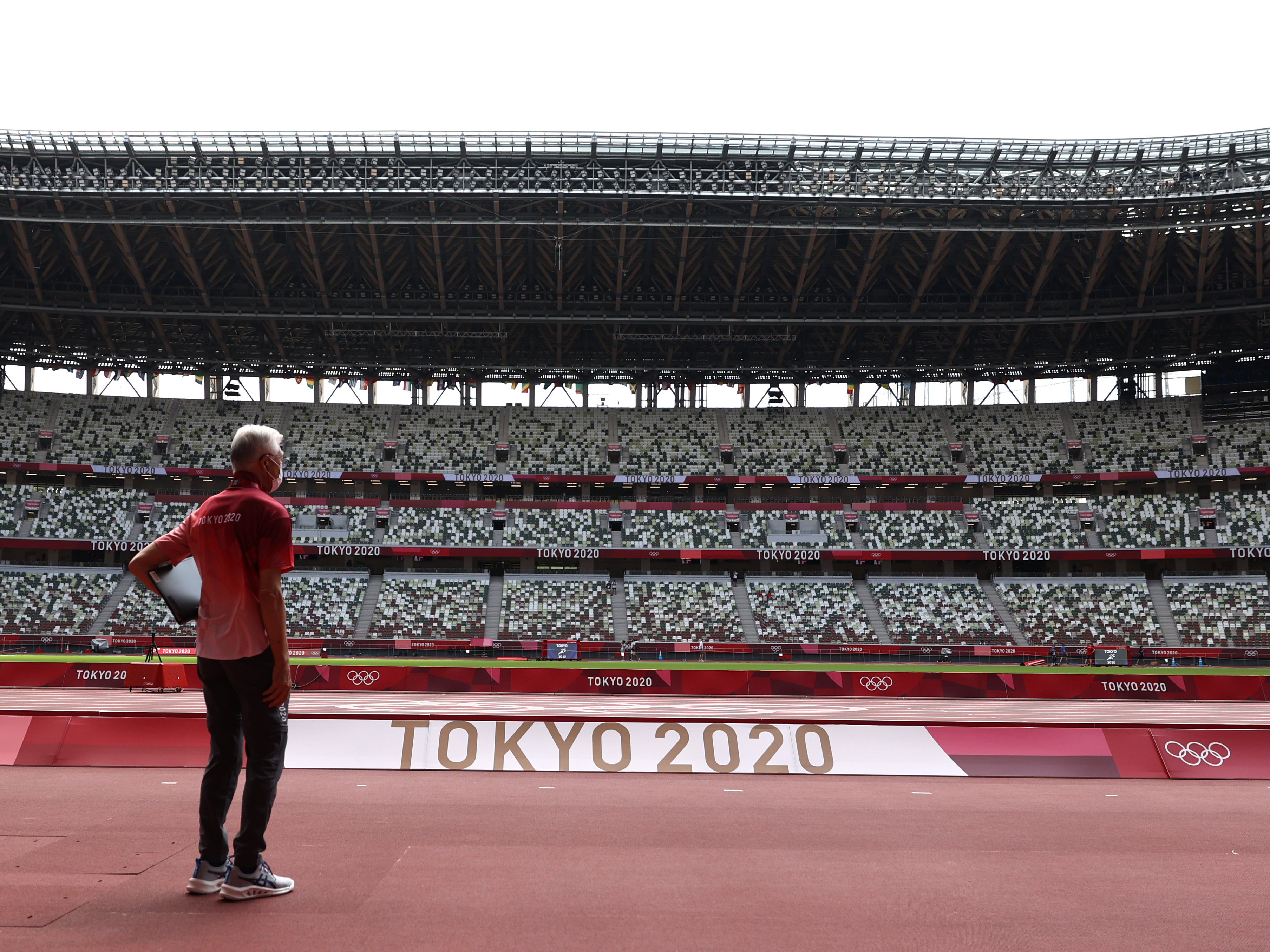 caption: A passerby looks on while wearing a protective face covering inside an empty Olympic Stadium, host to the Athletics competition, at the Tokyo Olympic Games on Thursday.