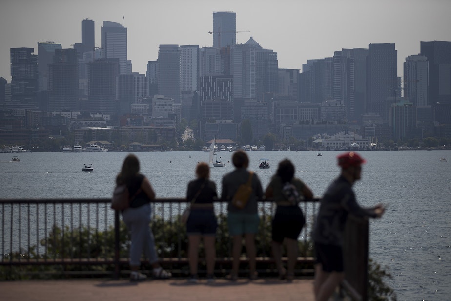 caption: People look toward a hazy Seattle skyline as wildfire smoke from Canada arrives in the area, on Thursday, August 12, 2021, at Gas Works Park in Seattle. 