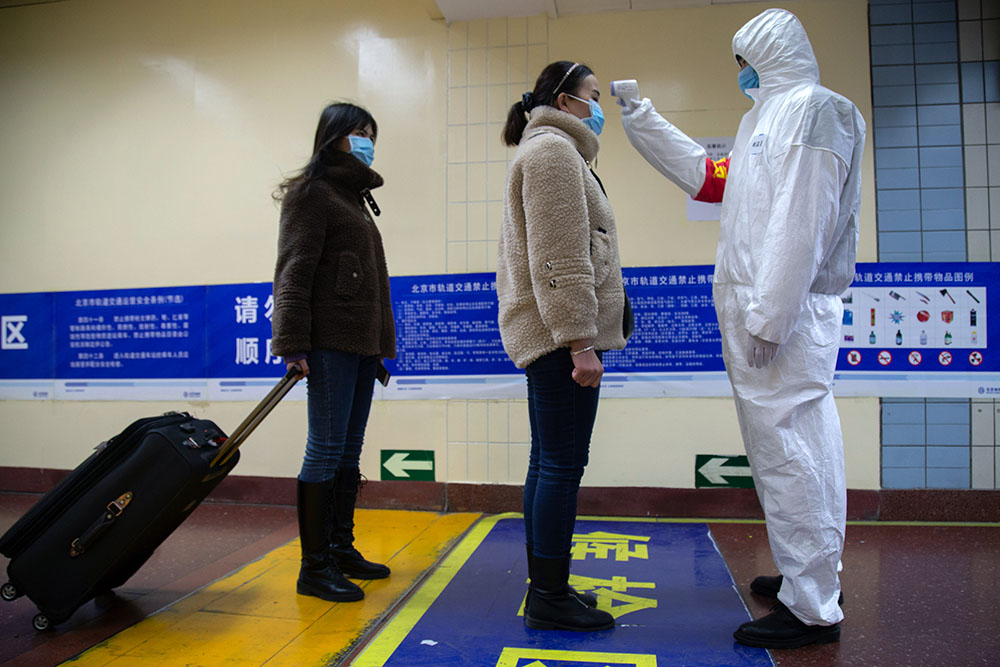 caption: A health worker checks the temperature of women entering the subway on January 26, 2020 in Beijing, China.  (Betsy Joles/Getty Images)