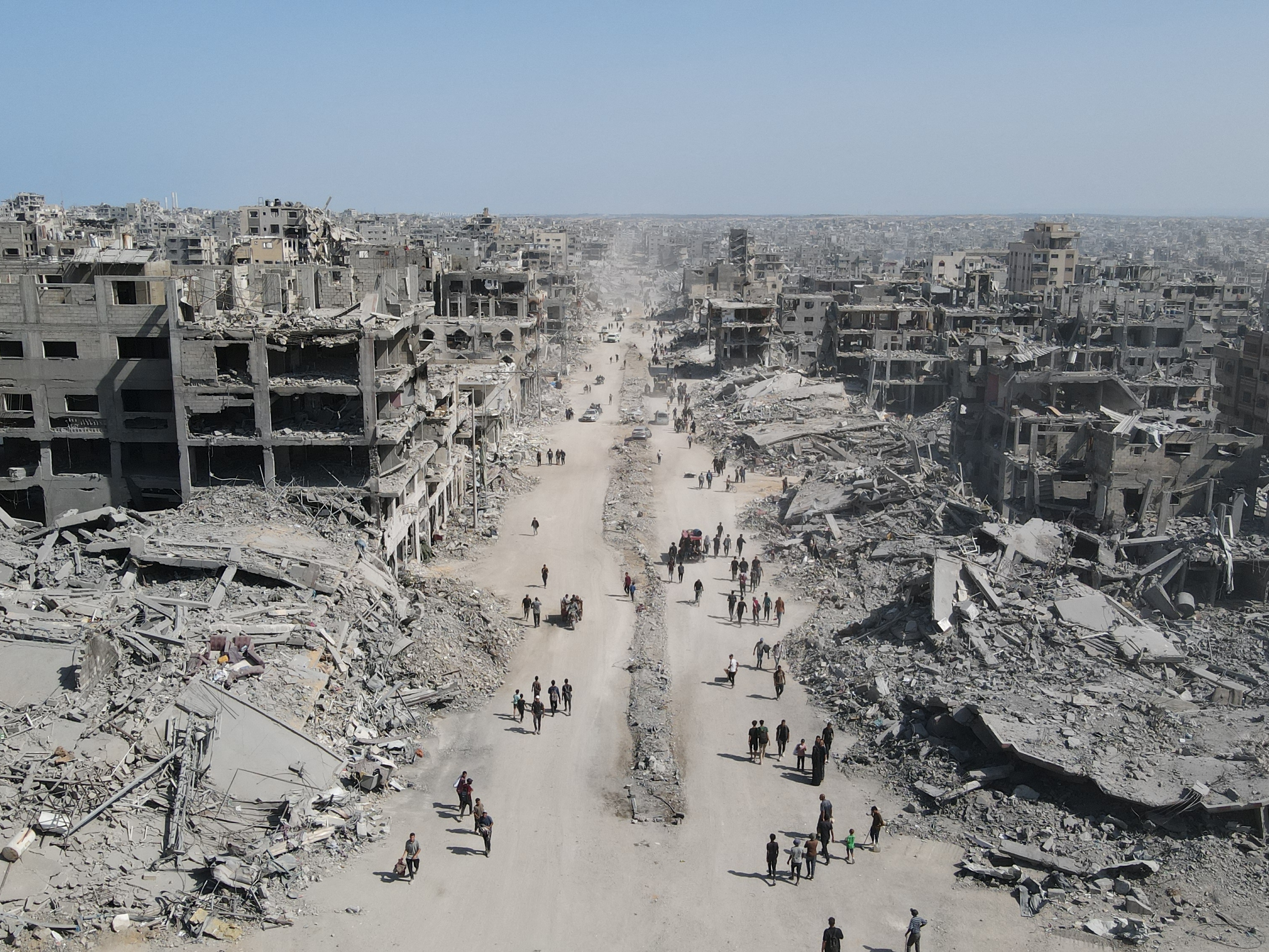 caption: People walk amid the destruction in Gaza City on Oct. 11, 2025, a day after a ceasefire took effect. Israel pulled back its forces on Oct. 10, and tens of thousands of Palestinians made their way back to their devastated homes.