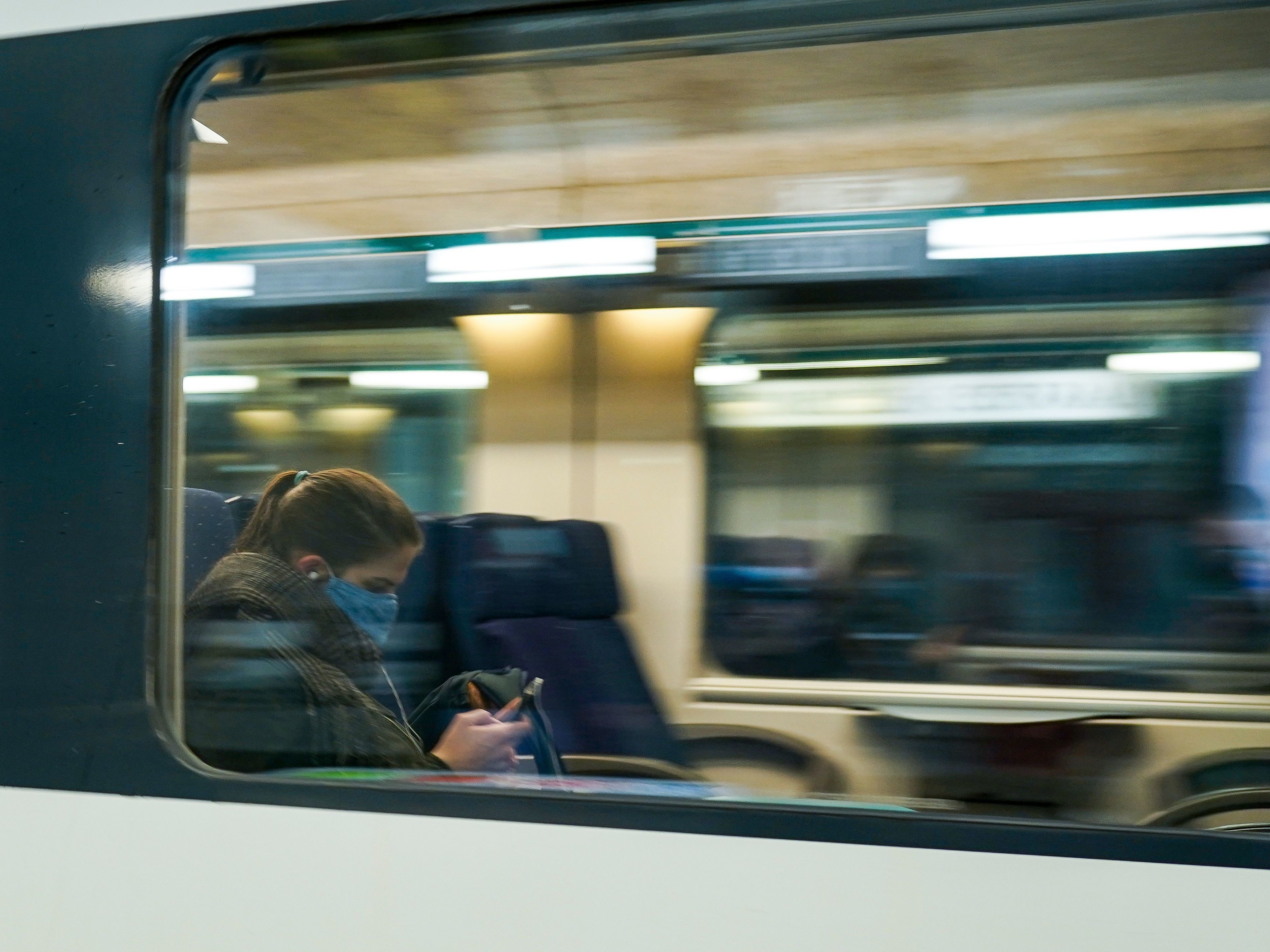 caption: A commuter wearing a protective face mask looks at her mobile phone in a train arriving at the Central Train Station in Brussels in May 2020. Belgium's new rule addresses the ever-blurry line between work and personal life in the pandemic.