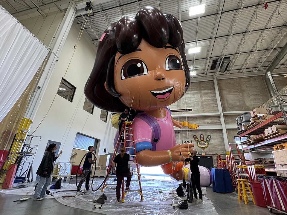 caption: The Dora the Explorer balloon gets pumped up for a flight over the streets of New York City in the 98th Macy's Thanksgiving Day Parade.