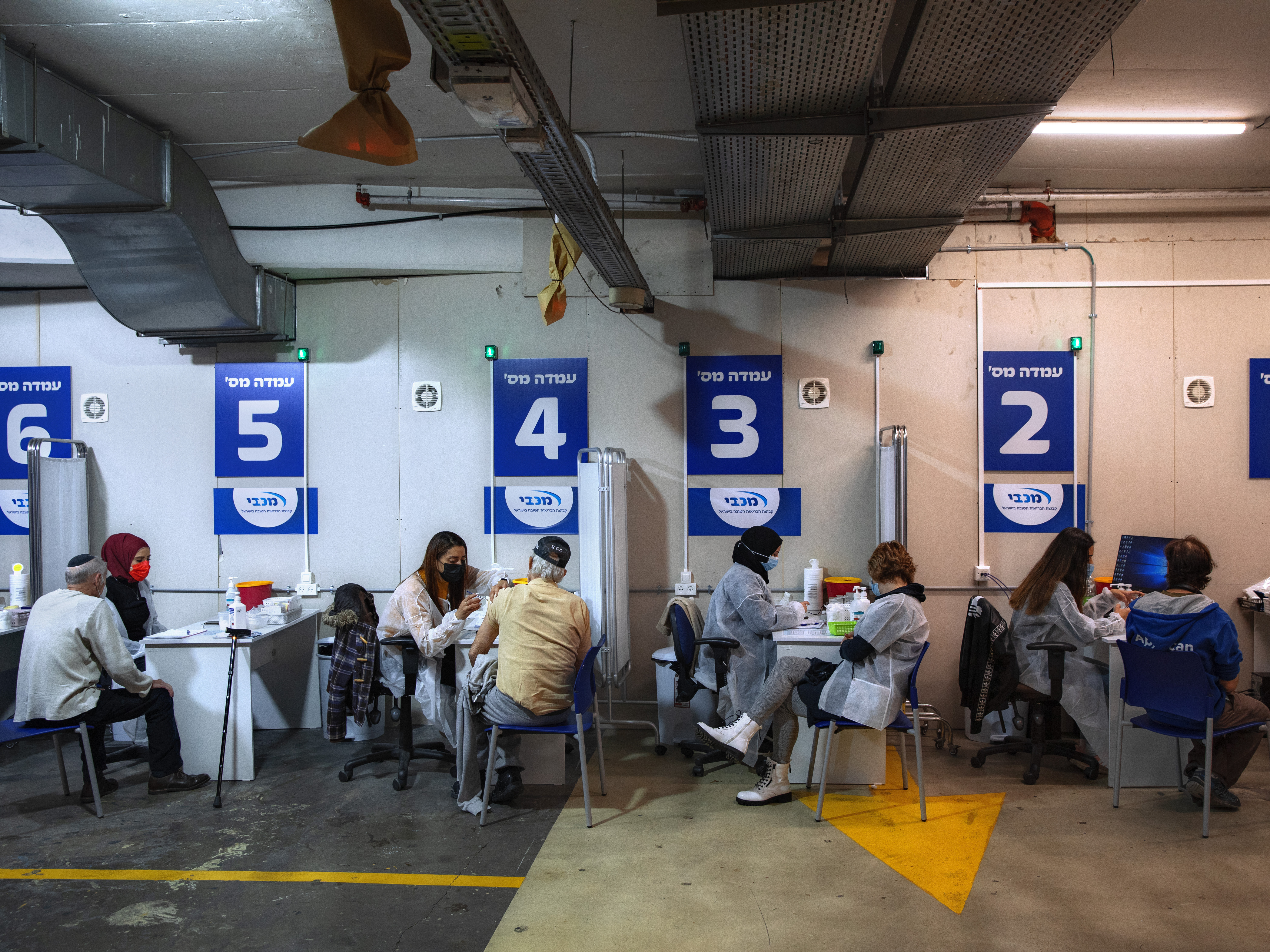 caption: Israelis receive a Pfizer-BioNTech COVID-19 vaccine from medical professionals at a vaccination center set up on a mall parking lot in Givataim, Israel, during a nationwide lockdown to curb the spread of the virus, on Jan. 20.