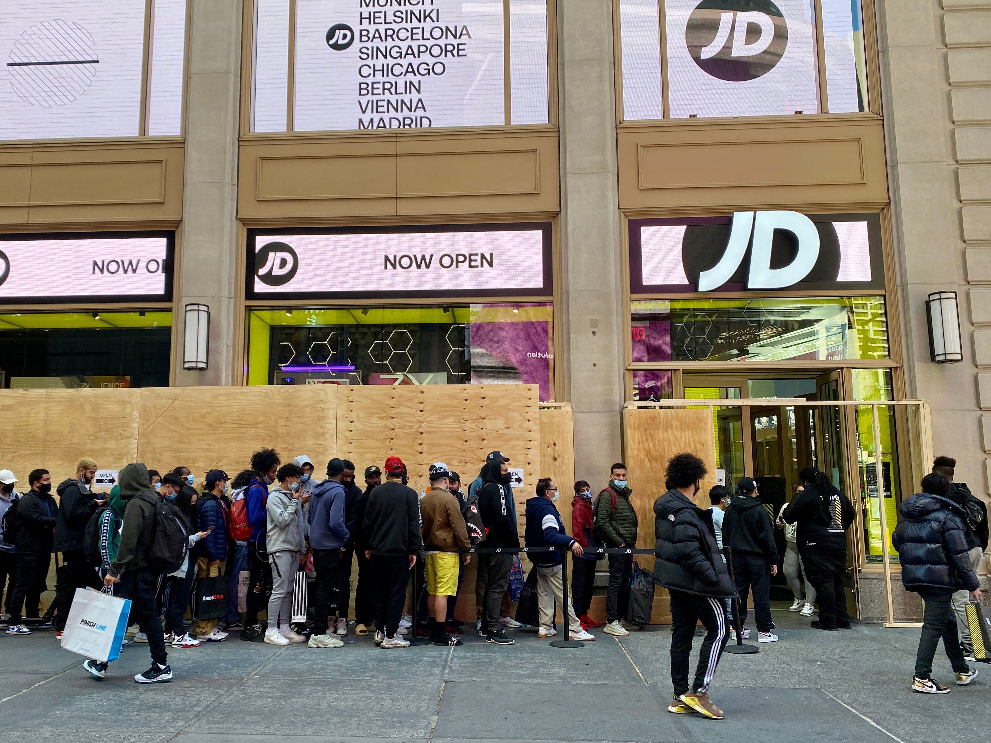 caption: People wait in line outside for their turn to enter the JD Sports store in New York City on Nov. 5.
