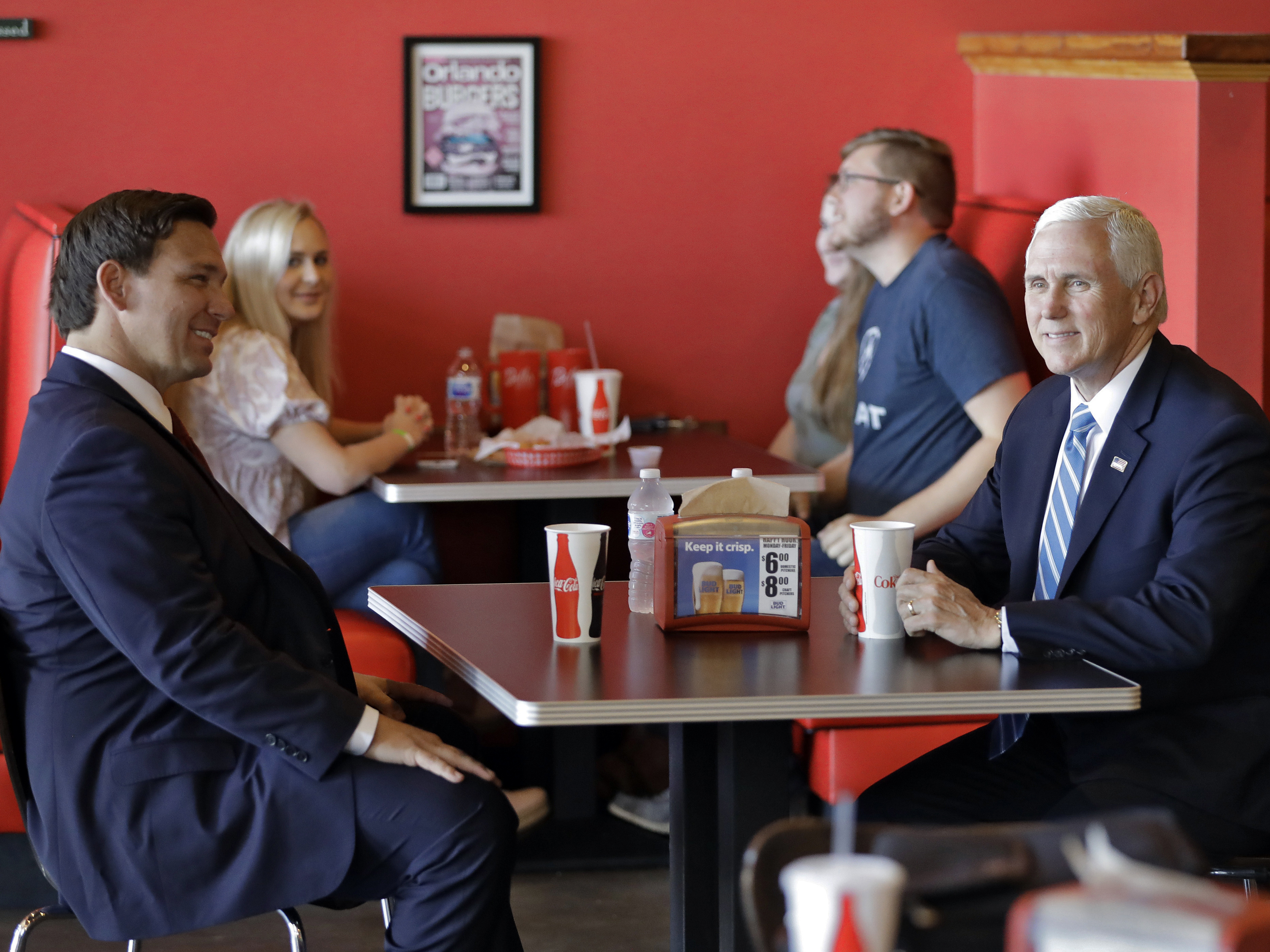 caption: Vice President Mike Pence, right, talks to Florida Gov. Ron DeSantis as they wait for their lunch at Beth's Burger Bar, Wednesday, May 20, 2020, in Orlando, Fla.