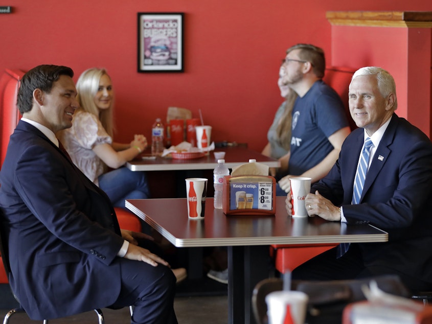 caption: Vice President Mike Pence, right, talks to Florida Gov. Ron DeSantis as they wait for their lunch at Beth's Burger Bar, Wednesday, May 20, 2020, in Orlando, Fla.
