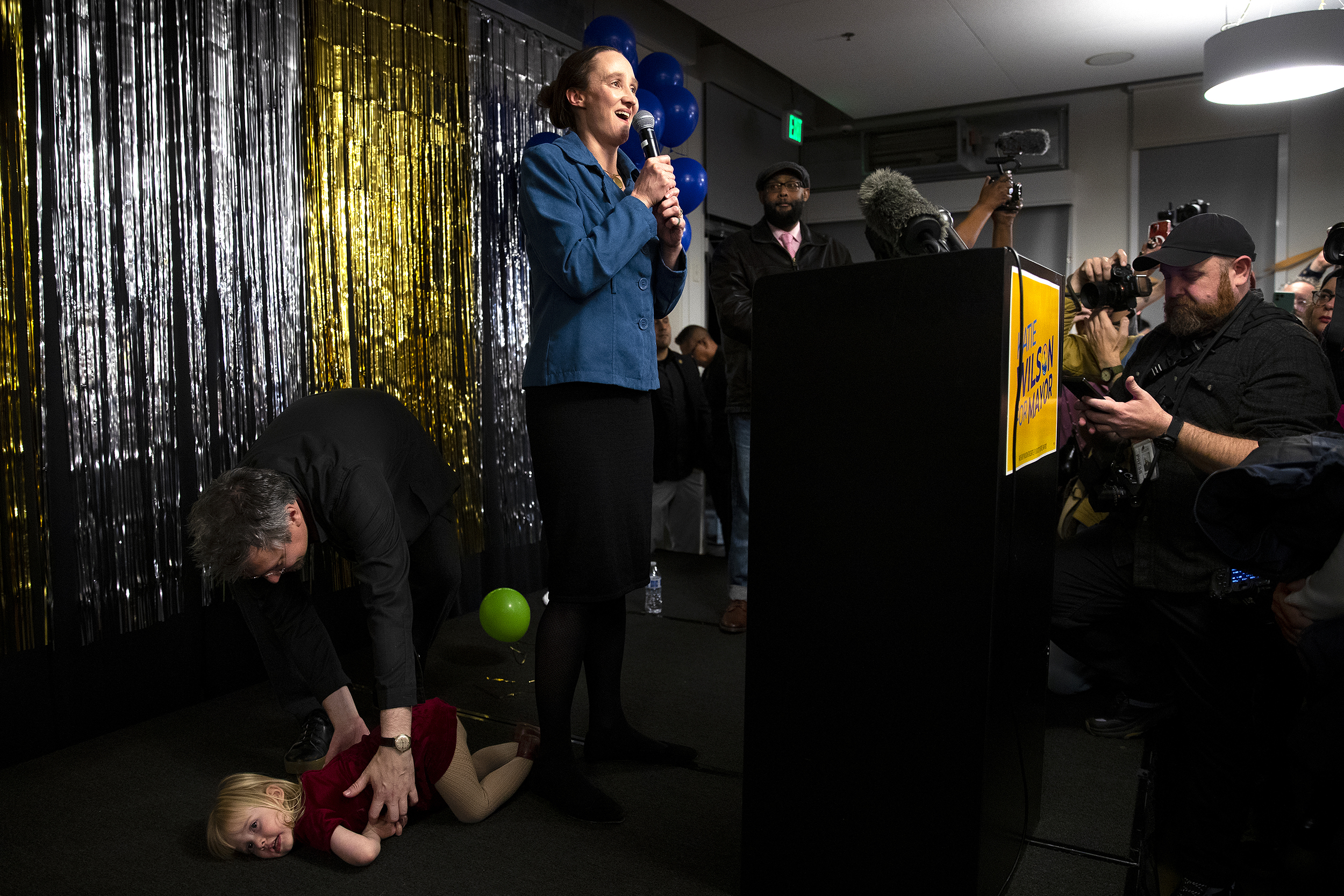 caption: City of Seattle mayoral candidate Katie Wilson speaks to supporters as her husband, Scott, picks up their two-year-old daughter Josie on stage, on Tuesday, November 4, 2025, at El Centro de la Raza in Seattle. "No one saw us coming," Wilson said later, giving credit for the win to her supporters and their efforts volunteering, posting on social media, holding house parties, and other activities. 
