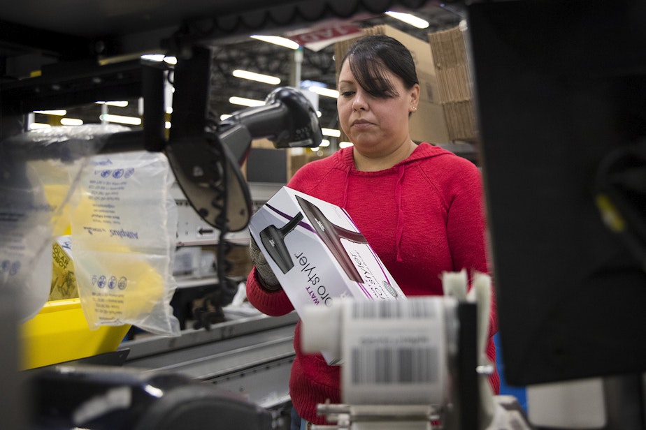 caption: Clara Vazquez scans items before putting them into boxes at an Amazon fulfillment center on Friday, November 3, 2017, in Kent.