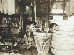 caption: A young Crescenciana Tan working as cashier at a local grocery store in the Philippines in 1960.